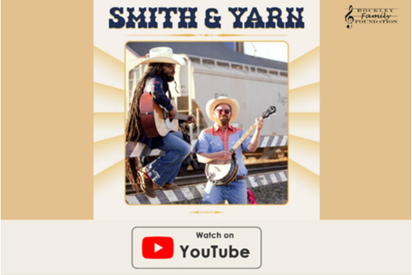 Two musicians in cowboy hats hold a guitar and a banjo in front of a train. 